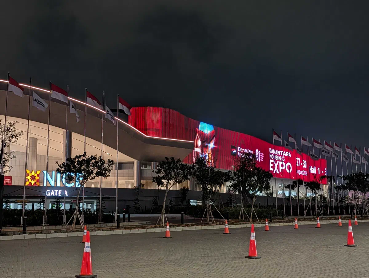 A convention centre at night, its curved facade wrapped in a red LED screen announcing a housing expo